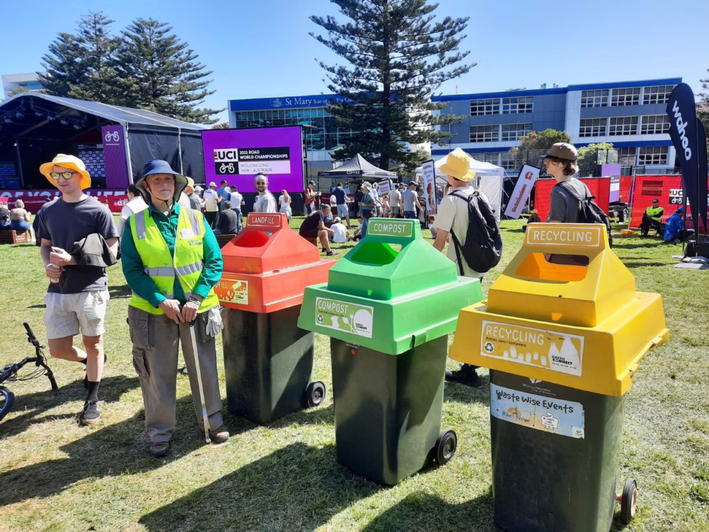 9npK4rSMY82eU9m3KgNwEXrQB6J3EEexfLIYFA Lady standing near a rubbish sorting station with three different bins